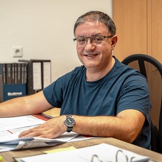Lächelnder Mann in einem modernen Büro bei der Arbeit Der Mann in einem blauen T-Shirt zeigt ein breites Lächeln, während er an einem gut organisierten Arbeitsplatz arbeitet.