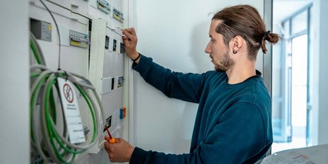 Ein Techniker arbeitet konzentriert an einem Stromverteiler, während er mit einem Werkzeug eine Anpassung vornimmt.