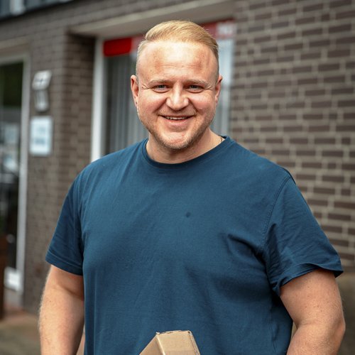 Vor einem Geschäft steht ein freundlicher Mann mit einem Paket, das er stolz in seinen Händen hält.