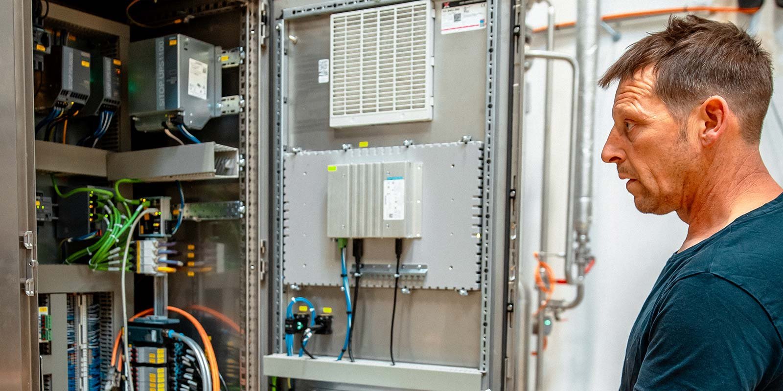 Ein Mann betrachtet konzentriert ein geöffnetes Schaltschrankgehäuse mit zahlreichen Kabeln und elektrischen Komponenten.