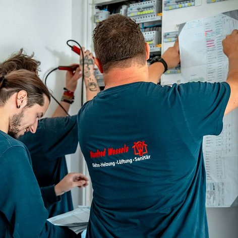 Zwei Techniker arbeiten konzentriert an einem elektrischen Schaltschrank, während sie Pläne und Werkzeuge verwenden.