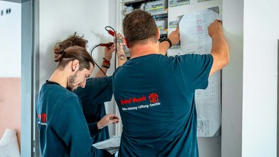 Zwei Techniker arbeiten konzentriert an einem elektrischen Schaltschrank, während sie Pläne und Werkzeuge verwenden.