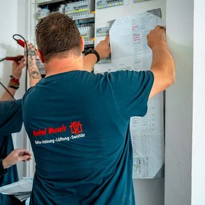 Zwei Techniker arbeiten konzentriert an einem elektrischen Schaltschrank, während sie Pläne und Werkzeuge verwenden.