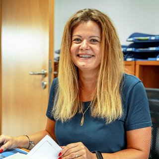 Lächelnde Frau am Schreibtisch mit Dokumenten Eine lächelnde Frau mit langen, blonden Haaren sitzt an einem Schreibtisch und hält Dokumente in der Hand.