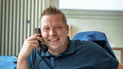 Lächelnder Mann am Telefon in modernem Büro Ein lächelnder Mann spricht am Telefon, während er an einem Schreibtisch mit Aktenordnern sitzt.