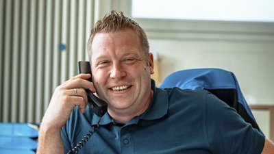 Lächelnder Mann am Telefon in modernem Büro Ein lächelnder Mann spricht am Telefon, während er an einem Schreibtisch mit Aktenordnern sitzt.