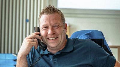 Lächelnder Mann am Telefon in modernem Büro Ein lächelnder Mann spricht am Telefon, während er an einem Schreibtisch mit Aktenordnern sitzt.