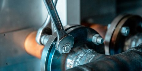 Ein verchromter Schraubenschlüssel greift eine metallene Verbindung, um eine präzise Anpassung an der Maschine vorzunehmen.