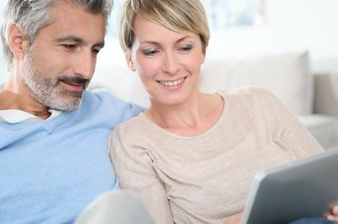 Ein Paaerchen sitzen nebeneinander und schauen auf ein Tablet